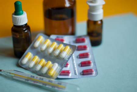 Medicines for colds, flu, viral diseases. Cough and cold remedies. Glass jars with syrup, colored tablets. Pills on a blue background. Antiviral drugs.の写真素材