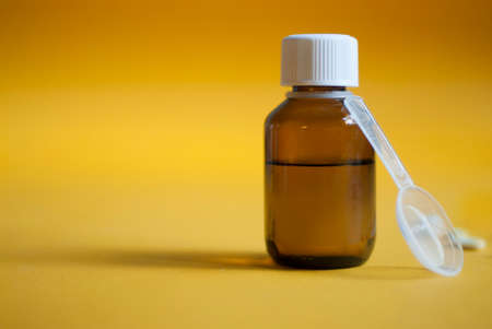 Cough syrup. Cold medicine. Pills and medicine on a yellow background. Pharmaceutical preparations for cough, flu, diseases. First aid kit. Syrup in a glass bottle.の写真素材