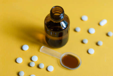 Cough syrup. Cold medicine. Pills and medicine on a yellow background. Pharmaceutical preparations for cough, flu, diseases. First aid kit. Syrup in a glass bottle.の写真素材
