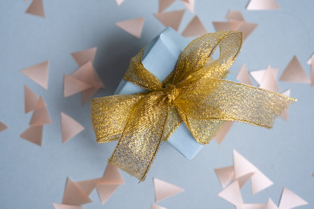 Blue gift box with gold ribbon. On a blue background with confetti. Gift for Valentines Day, New...