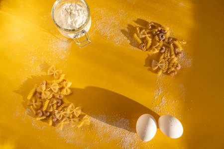 Assorted Italian pasta. On a yellow background. View from above. Pasta on a plate. Flour, eggs and pasta made from themの写真素材