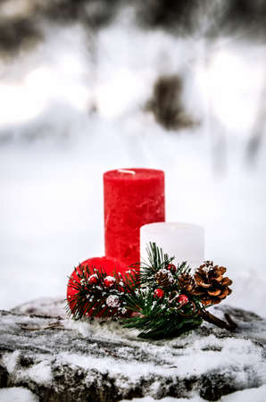 The composition of the three decorative candles and twigs with berries and cones on a snow-covered tree stump in the woods.の写真素材