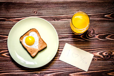 Breakfast consists of eggs in the form of heart, toast and juice. Next to the breakfast is a note with a declaration of love.の写真素材