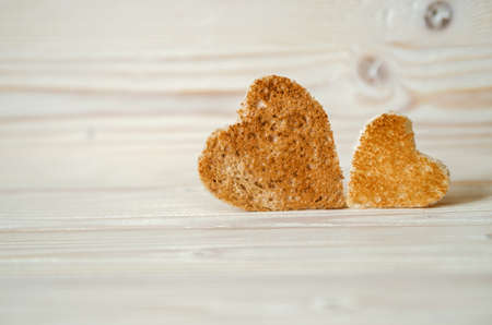 Two bread croutons in the form of hearts on a wooden stand on a white surface.の写真素材