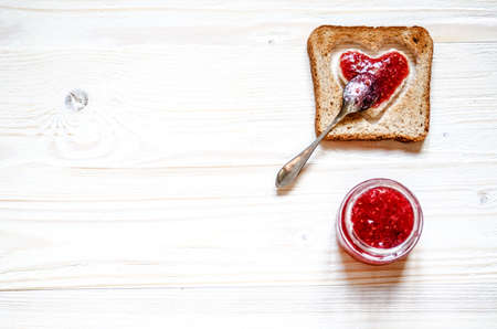 Toasted white bread, in which the heart of raspberry jam. Under the croutons is a jar of jam.の写真素材