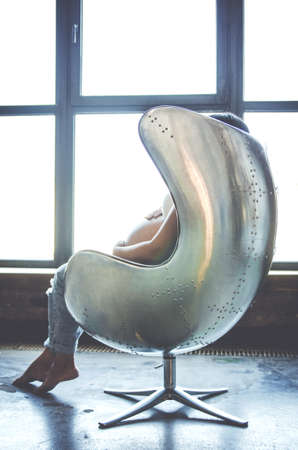 A pregnant girl sits in a chair and hugs her tummy.の写真素材