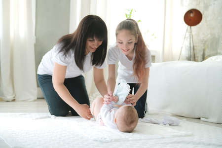 Mom and eldest daughter change the diaper of a newborn baby.の写真素材