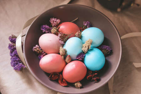 Close up on colorful pastel colored Easter eggs on a brown plate, decorated with dry flowersの写真素材