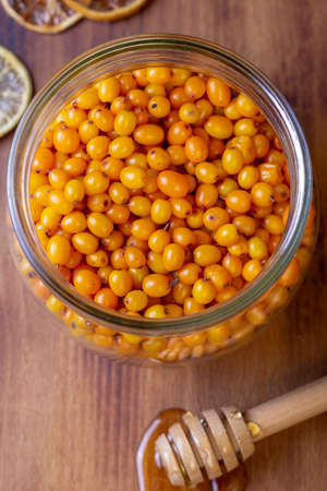 Fresh sea buckthorn in glass with honey. The view from the top. Organic berries on wooden...