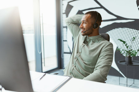 Smiling african businessman working on computer while sitting in modern office and looking at side