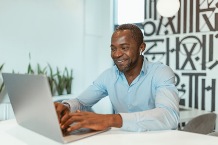 Smiling african businessman working on laptop while sitting in modern office