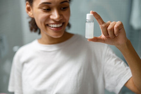 Close up of smiling girl holding natural skincare or body care cosmetics standing in bathroomの写真素材