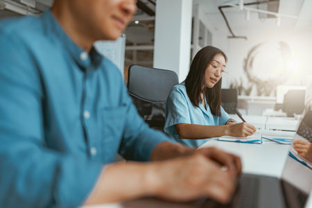 Smiling asian businesswoman working on computer sitting in coworking on colleagues backgroundの写真素材