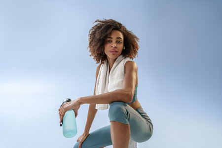 Woman with bottle of water after exercising, resting and looking at side on studio backgroundの写真素材