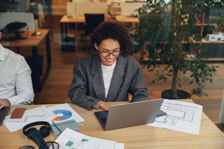 Smiling woman manager working on laptop in modern coworking while sitting near colleagues