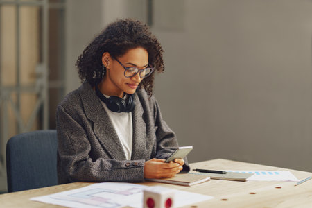 Young woman architect use phone sitting in cozy coworking during working dayの写真素材