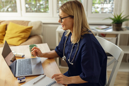 Female healthcare worker doing some paperwork and using laptop while working at doctors officeの写真素材