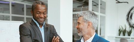 Two happy businessmen talking about deal standing in meeting room in modern officeの写真素材