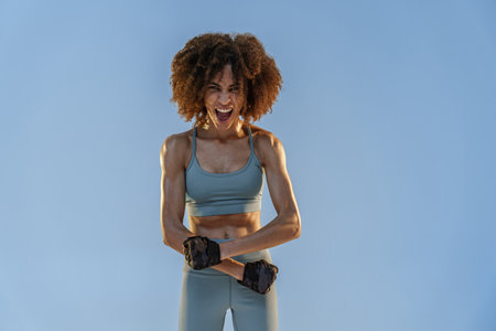 Sporty woman flexing muscles with energy to show off her biceps and strong abs on studio backgroundの写真素材