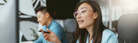 Smiling asian businesswoman working on computer sitting in coworking on colleagues backgroundの写真素材