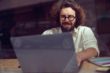 Smiling male freelancer working on laptop while sitting in modern coworking. Remote work conceptの写真素材