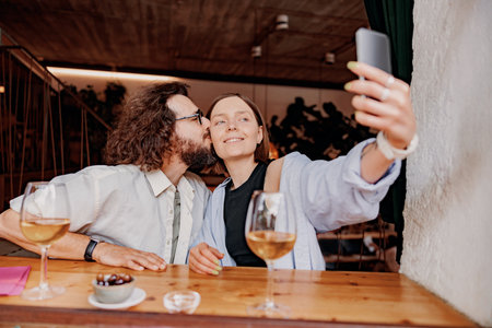 Man kissing woman in a cheek and take a selfie while they drinking wine in bar during romantic dateの写真素材