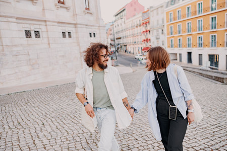 Smiling romantic hipster couple in love holding hands while walking on old city street in Lisbonの写真素材