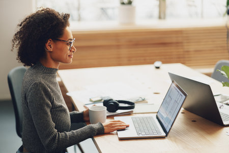 Young woman manager drinking coffee while working on laptop in coworkingの写真素材