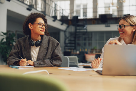 Two smiling women freelancer talking during working day in coworking