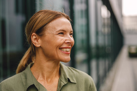 Close up of smiling woman entrepreneur standing on modern building background and looking at sideの写真素材
