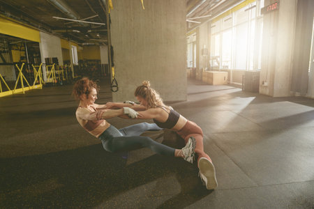 Professional trainer helping woman to sitting on straddle split on floor in gym