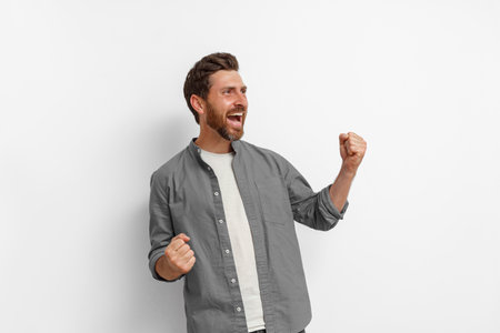 Expressive smiling man standing on white background and screaming with rise arms