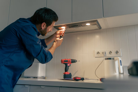 Professional male worker in uniform repairing modern cooker hood in kitchenの写真素材