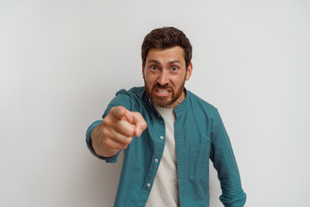 Indignant man standing over white background pointing displeased and angry to you on cameraの写真素材