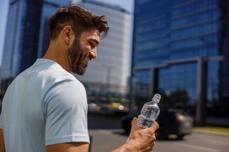Smiling sport man holding water bottle after running in the city skyscrapers backgroundの写真素材