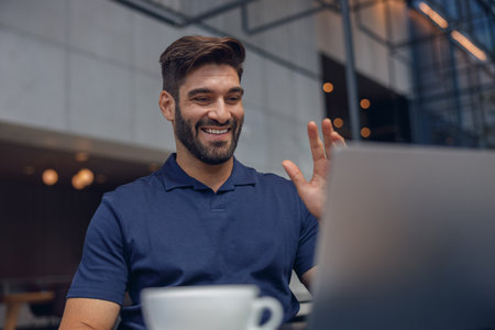 Businessman have video conference with colleague and waving Hi while sitting in cozy coworkingの写真素材