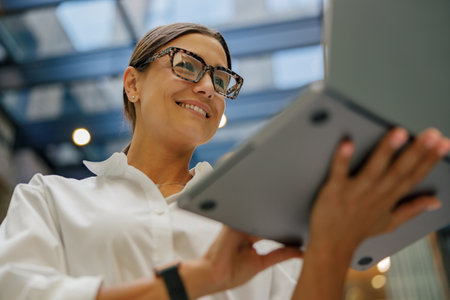 Stylish business woman in eyeglasses working on laptop standing on modern office backgroundの写真素材