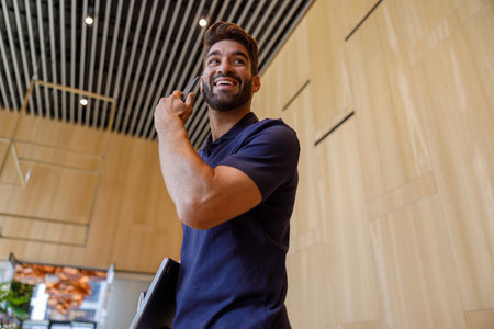 Bearded smiling businessman talking by phone when entrance office with laptop and looks away