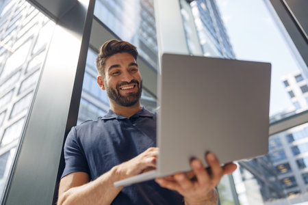 Handsome entrepreneur working on laptop standing in modern coworking near windows during working day