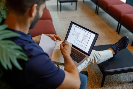Close up of male architect is making notes in note pad during work on laptop in coworking spaceの写真素材
