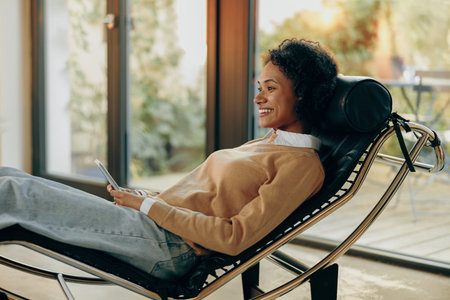 Smiling young woman is using mobile phone while lying on sofa at home and have a rest