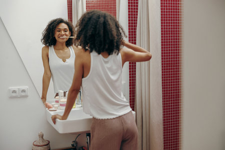 Positive woman brushing teeth with toothbrush standing near mirror In bathroom. Oral hygiene conceptの写真素材