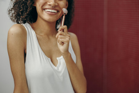 Close up of woman at bathroom use facial roller for skin care in front of mirror. Skin care conceptの写真素材