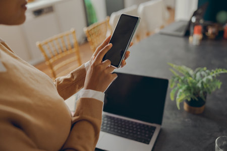 Close up of female freelancer is use mobile phone while working on laptop from homeの写真素材
