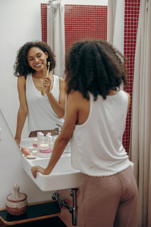 Young woman brushing teeth with toothbrush in the morning and looking in mirror in bathroomの写真素材