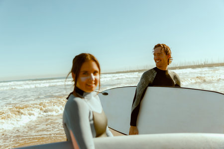 Two happy surfers in wetsuit with his surfboards entering out of sea after surfing on wavesの写真素材