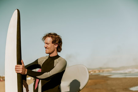 Male surfer in wetsuits standing with surfboard and preparing for ride on wavesの写真素材