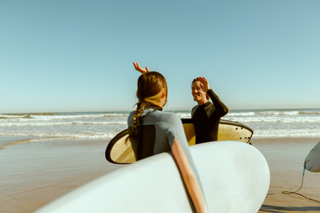 Surfer meets friend by waving hand while carrying surfboard on the beachの写真素材