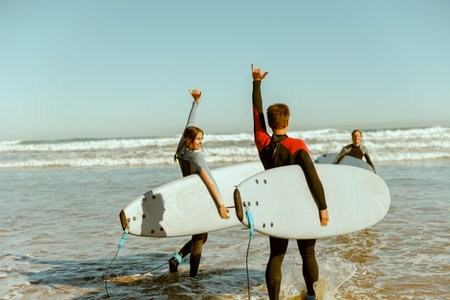 Surfers meets friend by waving hand while carrying surfboard on the beachの写真素材