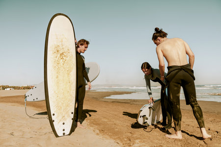 Surfers in wetsuits standing on beach with surfboards and preparing for ride on wavesの写真素材